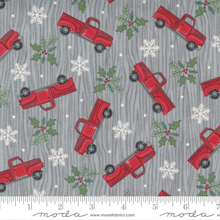 Tossed red trucks, mistletoe, white snowflakes on grey wood background 